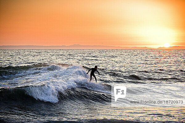 A young man surfing at sunset.