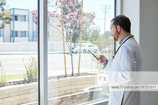 Side view of male doctor using smart phone while standing near window