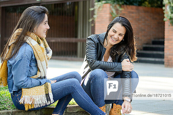 Happy friends talking while sitting on the street