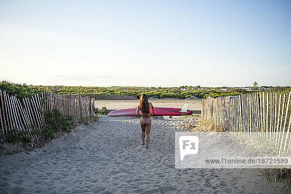 Woman in skimpy bikini walking with her surfboard at sunset