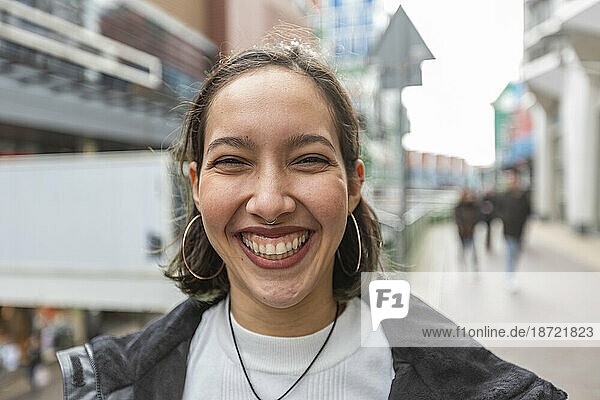 Mixed race woman with wide smile standing on street in city.