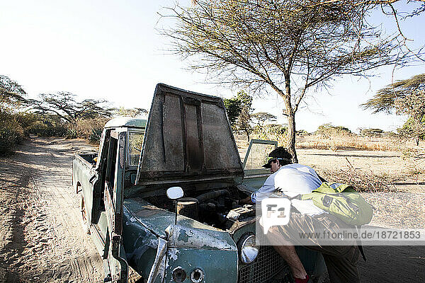 A man looks inside a beat up old car after it breaks down in a rural stretch of desert.