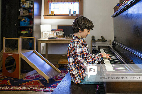 side view of a child sitting in window light practicing piano