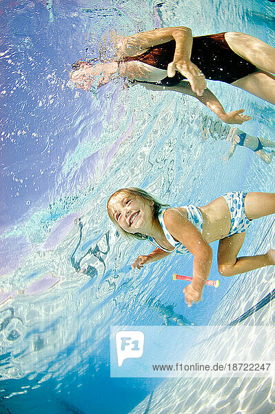 A young girl underwater as she learns to swim in a pool with her mother.