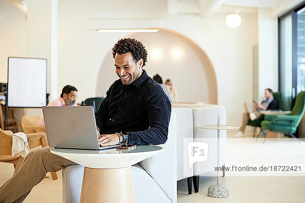 Smiling male entrepreneur working on laptop while sitting on sofa