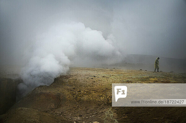 Woman stands near geyser in a foggy desert in Bolivia