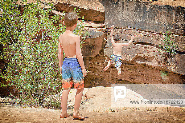 Young boy jumps off cliff face (facing away from camera) near Moab  UT