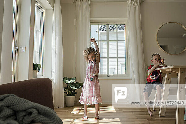 young girl dancing a home whilst her brother plays
