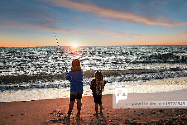 Two little girls fishing in the ocean at sunset