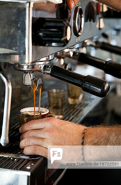 Detail of an espresso machine and man holding a cup.