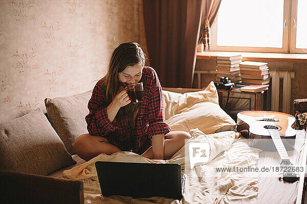 Happy teenage girl drinking tea in bed