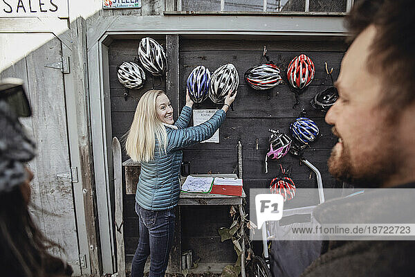 A young woman grabs two bike helmets hanging on a wall