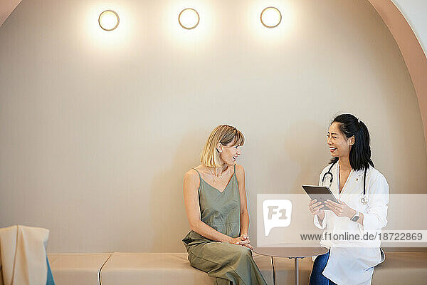 Smiling doctor discussing with female colleague sitting in hospital