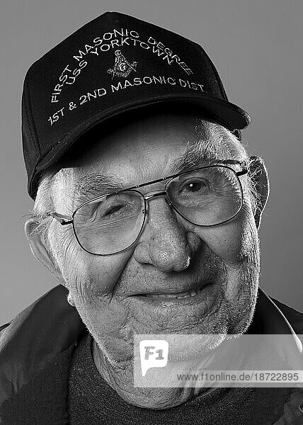 An older veteran man wears a war related hat and glasses for a portrait.