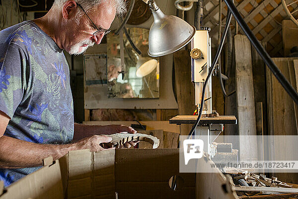 Side view of an elderly man inspecting handiwork in workshop