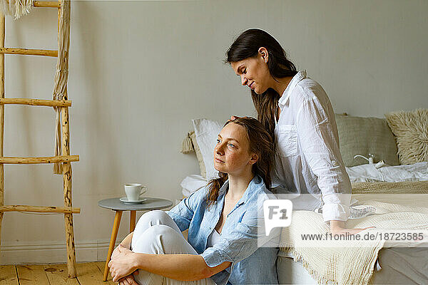 Two young women sitting together at home  one brushing another's hair