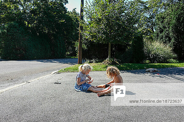two children sitting on driveway playing in the sunlight