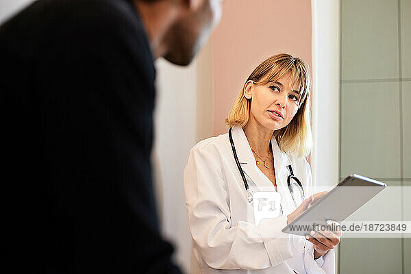 Blond female doctor holding tablet PC while looking at male patient