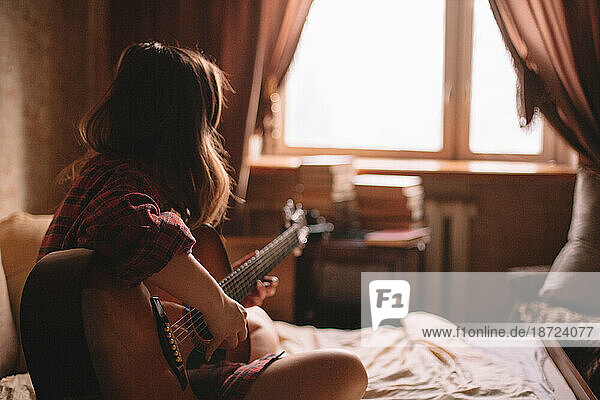 Teenage girl playing guitar at home