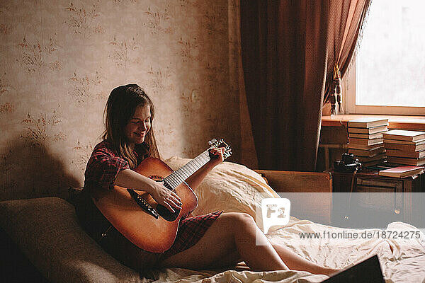 Teenage girl playing guitar at home