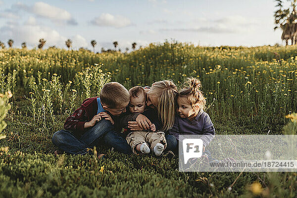 Four siblings smiling at each other in field of flowers with blue sky