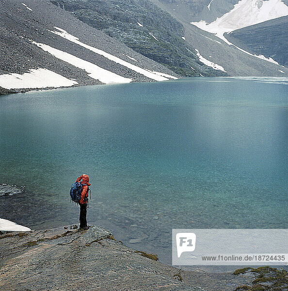 A hiker stands on the shore of a glacial lake.