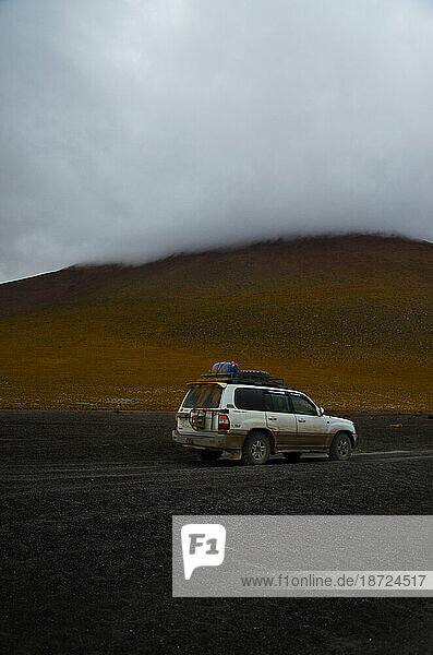 Muddy car in front of mysterious cloudy mountain in Bolivia