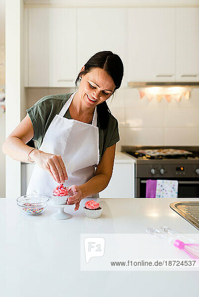 A baker woman smiling as she decorates a pink cupcake