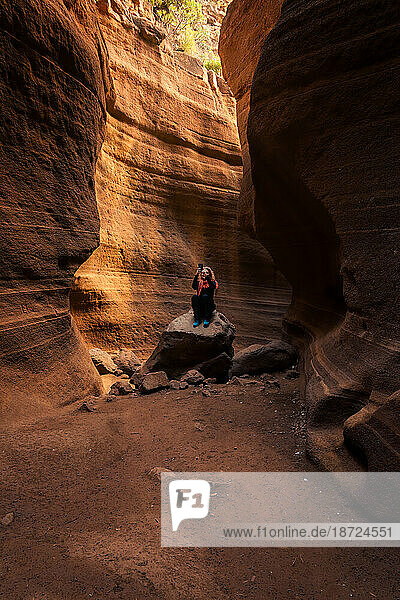 unrecognizable woman taking a picture on a rock inside a canyon