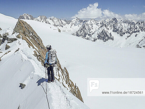 A woman mountaineer looks back from an exposed snow ridge in the Alps