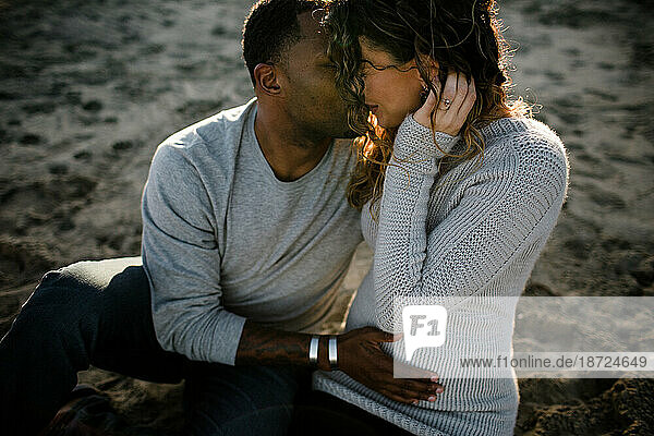 Multi racial couple embrace on beach at sunset