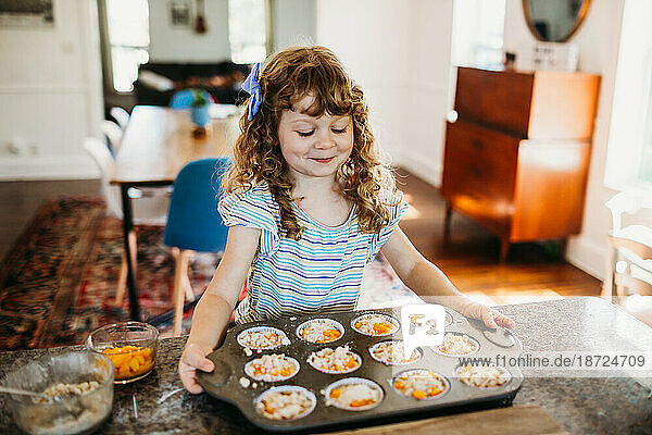 Young girl holding tin of fresh peach muffins ready to put in oven