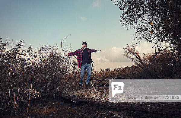 handsome man is walking on an overturned tree
