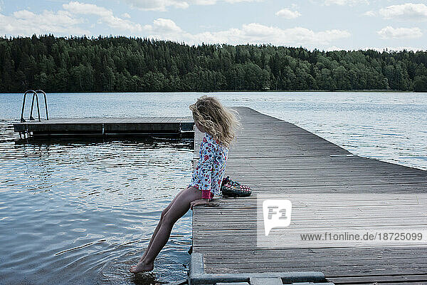 young girl sitting on a jetty looking at the water