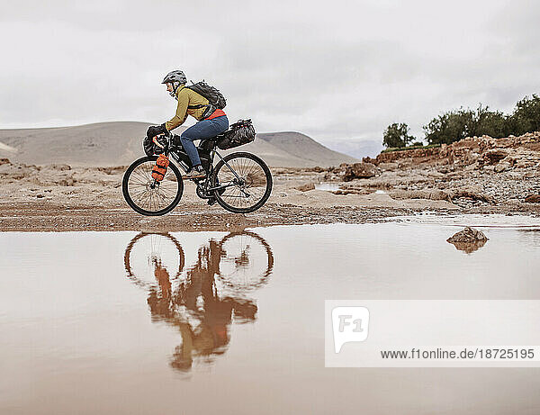 A female cyclist is reflected in muddy water  Atlas Mountains  Morocco