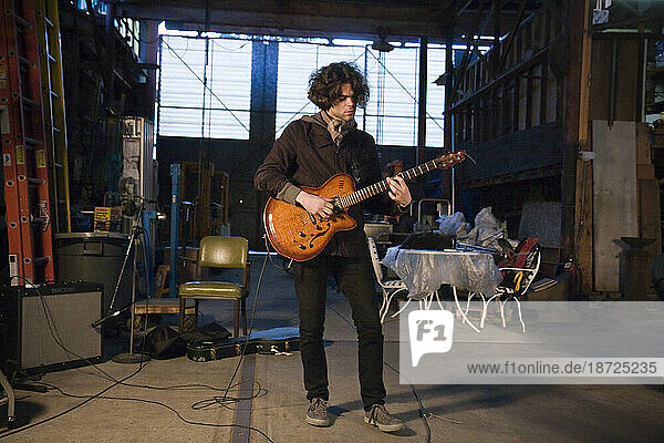 A young man plays electric guitar during a recording session in a warehouse in Seattle  Washington.