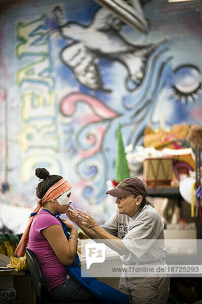 A woman creates a mask on a girl for a parade in Santa Barbara. The parade features extravagant floats and costumes.