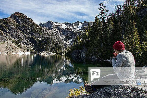 Hipster hiker girl eats breakfast by wild mountain lake in Washington