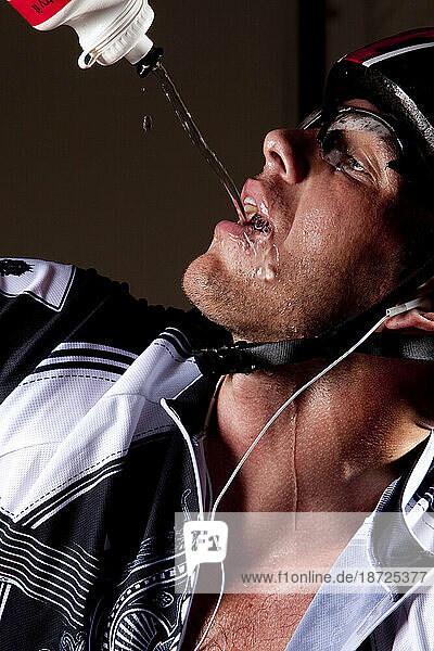 A biker pours water into his mouth from a squeeze bottle.