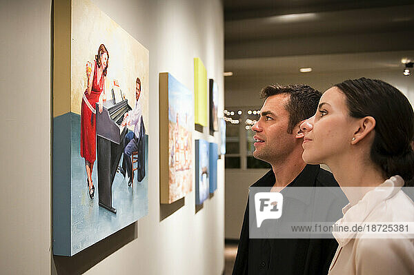 A couple take a close look at a painting in a gallery.