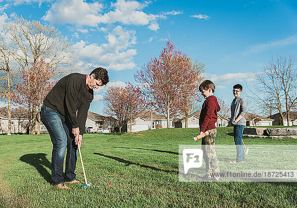 Father and his two boys playing croquet together in a park setting.