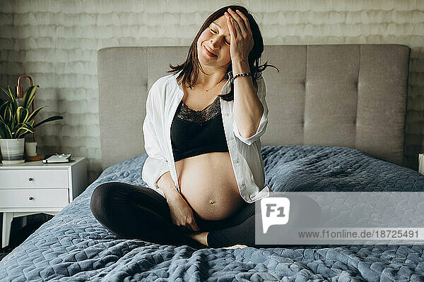 Pregnant girl sitting on the bed with her eyes closed