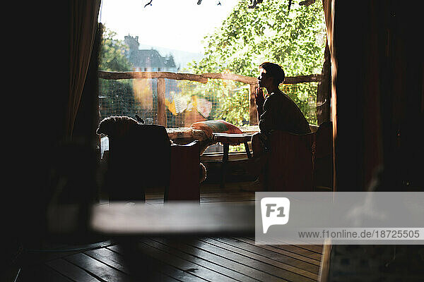person enjoys warm sunlight in window of wooden treehouse
