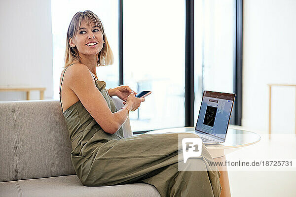 Smiling businesswoman looking away while sitting on sofa at cafe