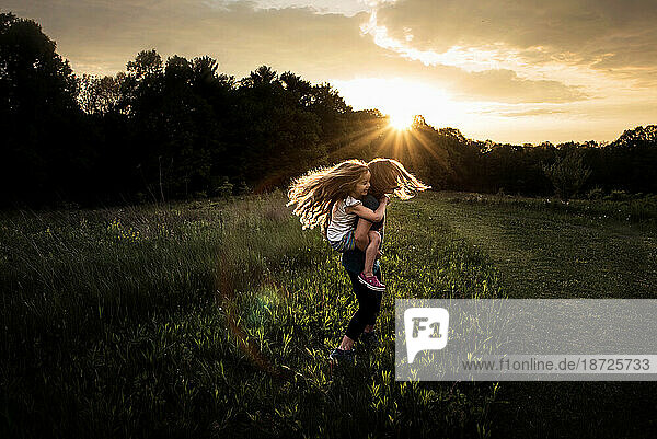 Young girls twirling in grassy field at sunset
