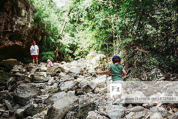 Young boy and girl climbing rocks while hiking with dad.