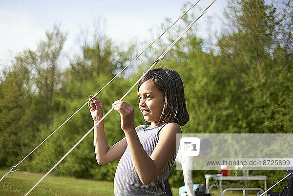 Young Asian girl playing with tent lines on a camping site
