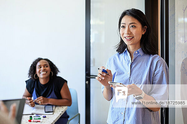 Smiling female entrepreneur holding smart phone and felt tip pen