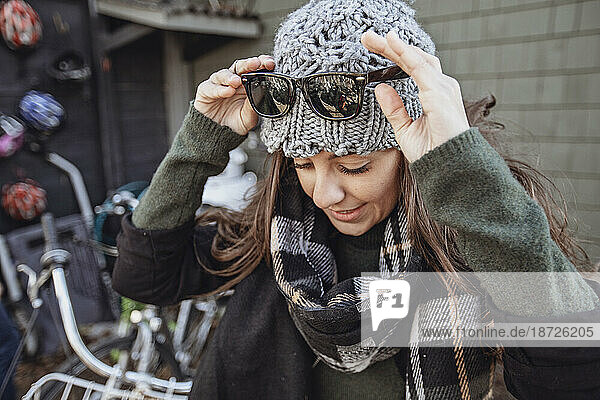 a young woman with a hat and scarf adjusts her sunglasses