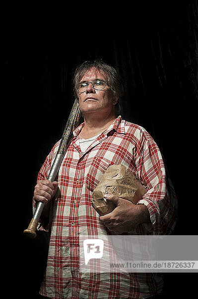 A middle aged Canadian man wearing a plaid shirt carries his baseball bat and lunch while standing in a studio built on the sidewalk on the corner of Broadview Avenue and Gerrard S